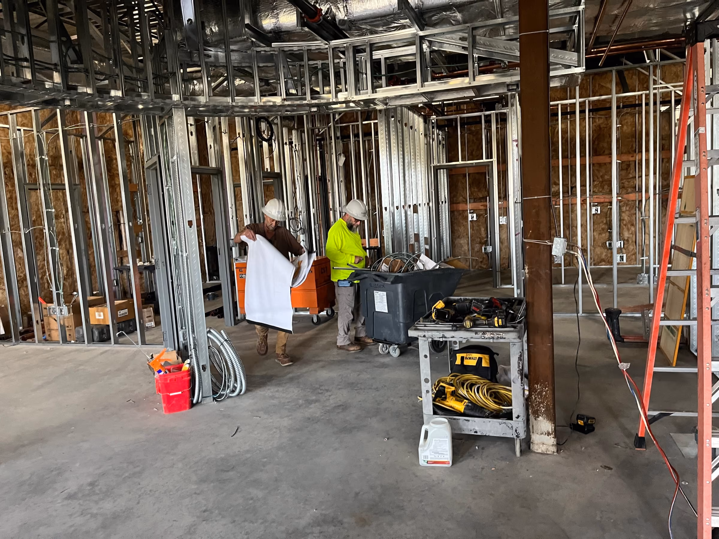 Two workers reviewing drawings on site inside a building framed out in metal stud